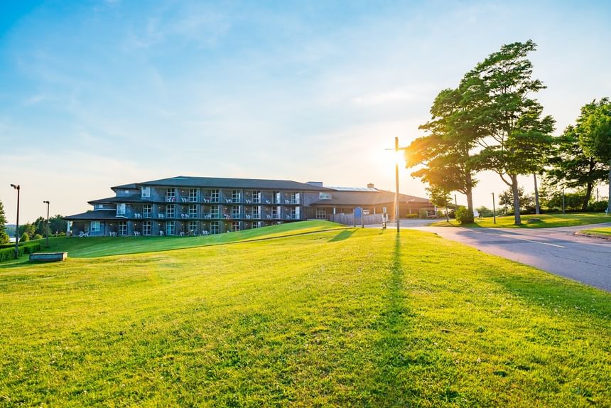 Resort exterior surrounded by expansive green lawns under a golden sunset glow at Rodd Brudenell River Resort