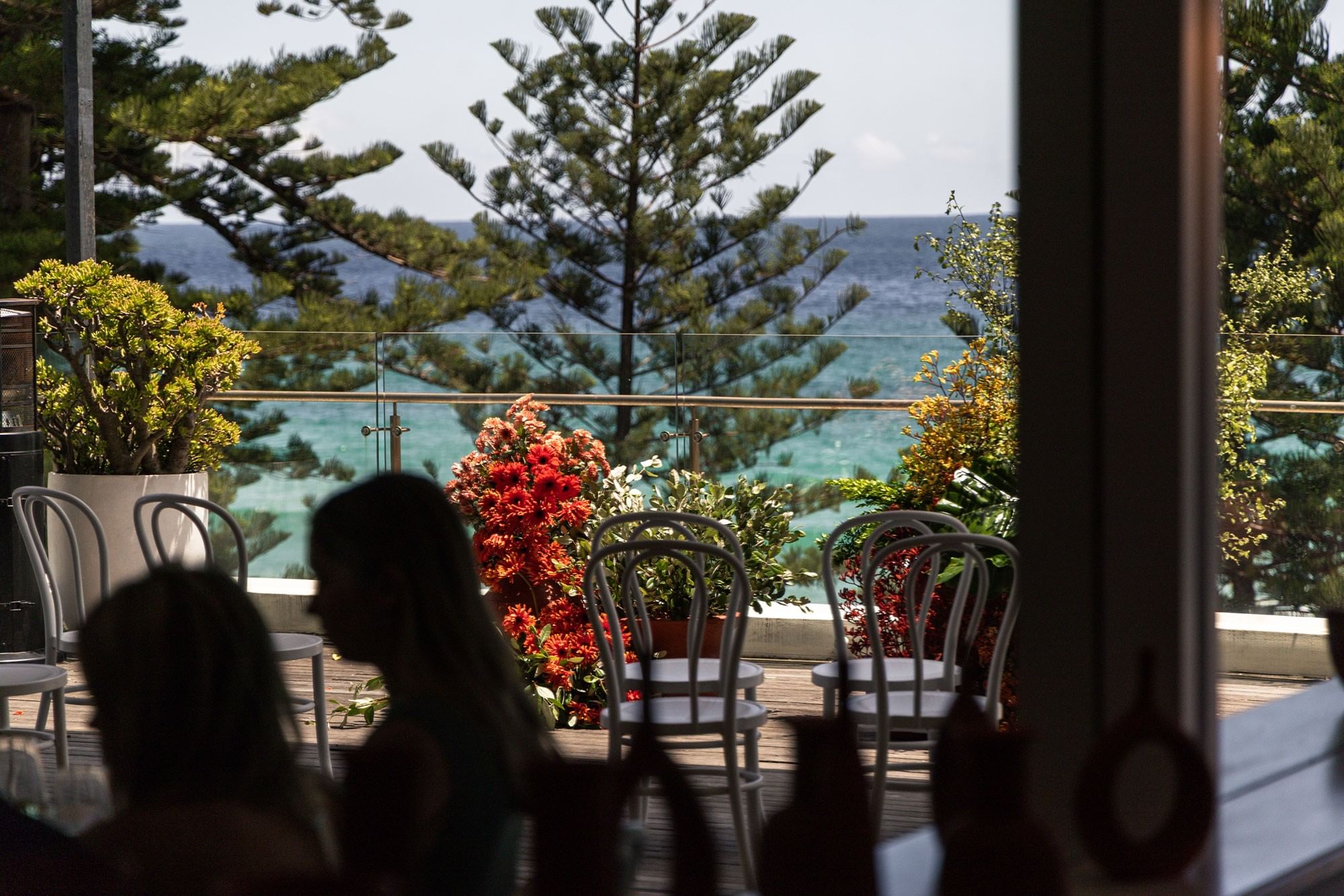 Elysium Manly wedding terrace viewed from inside featuring guests gathered near floral arrangements overlooking the sea