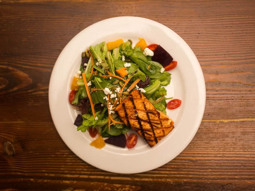Plate of grilled salmon and mixed salad on a wooden table at Pickwick San Francisco.
