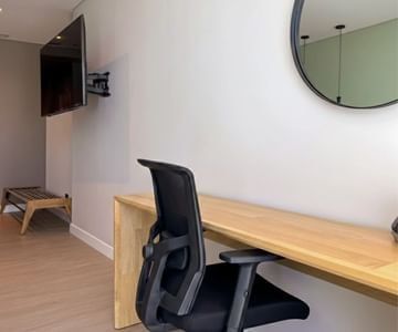 Long wooden work desk with office chair beneath wall-mounted television and round mirror in a suite at Hotel B3 Sibelius