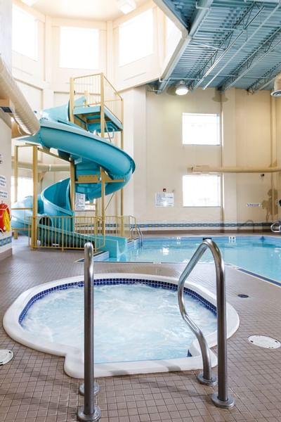 Tiled hot tub with metal railings by an indoor pool, under a spiral blue water slide at Glenmore Inn & Convention Centre