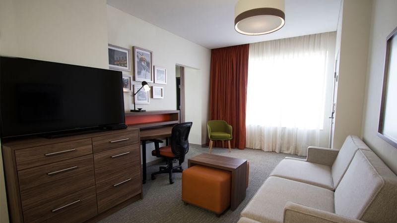 Modern living room featuring a gray sofa, desk, TV, and a chair at Fiesta Inn Suites Aeropuerto del Bajío