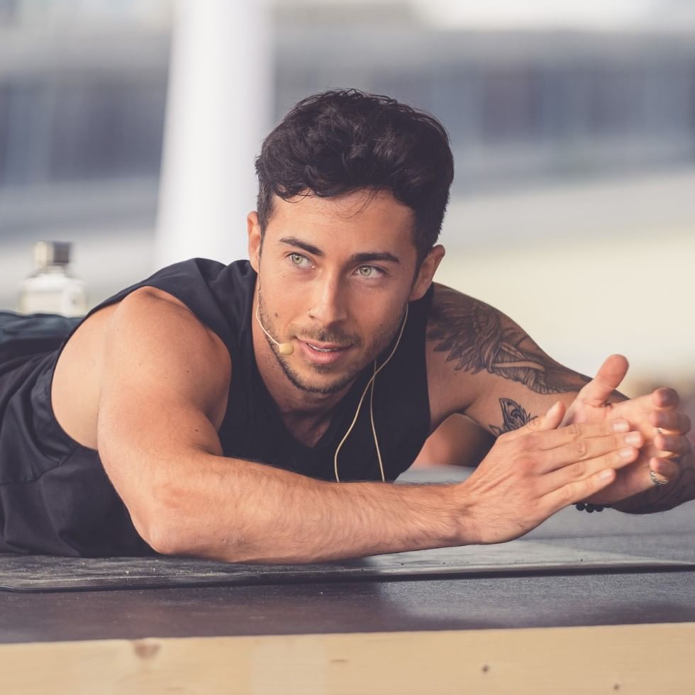Muscular man lying on exercise mat with earphones, smiling for fitness event.