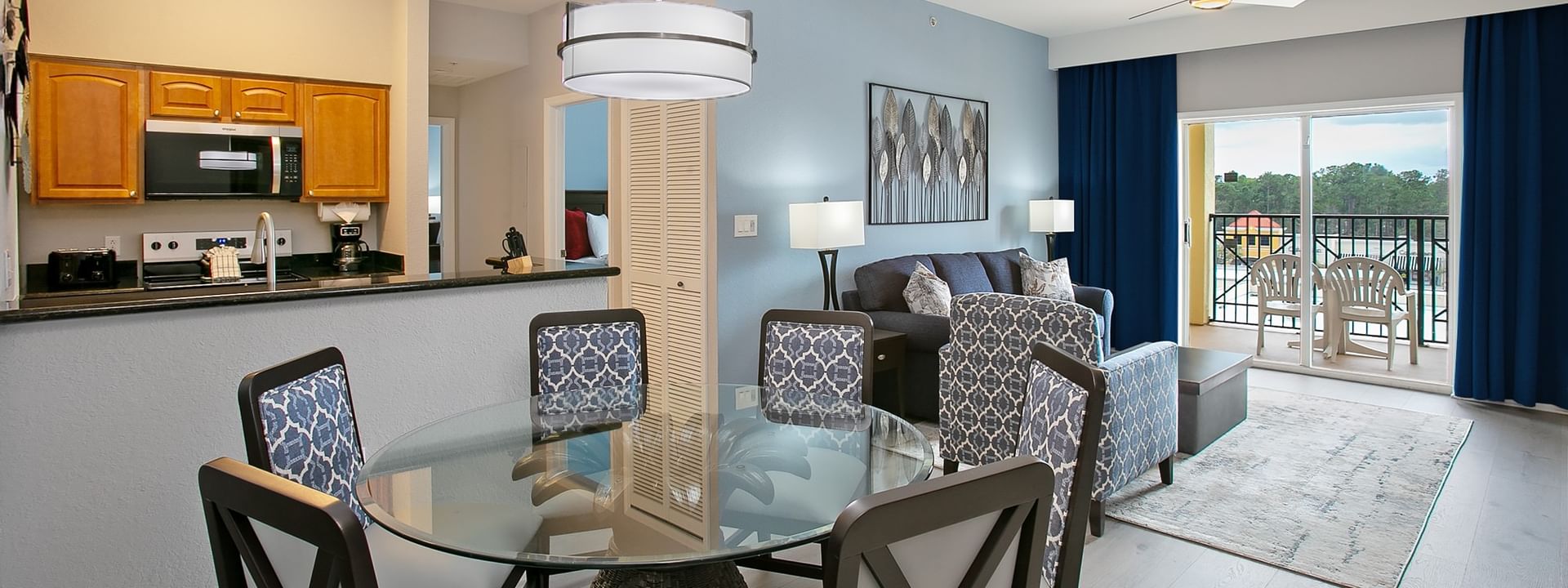 A wide view of a suite with a kitchenette, dining table, sofa, and balcony.