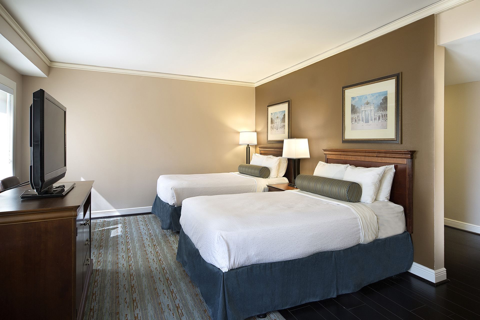A hotel room with two beds, a TV, and a lamp.