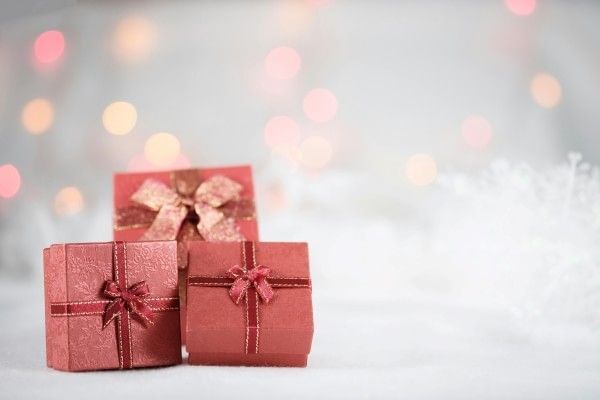 Three presents wrapped in red paper with faded twinkling lights in the background.