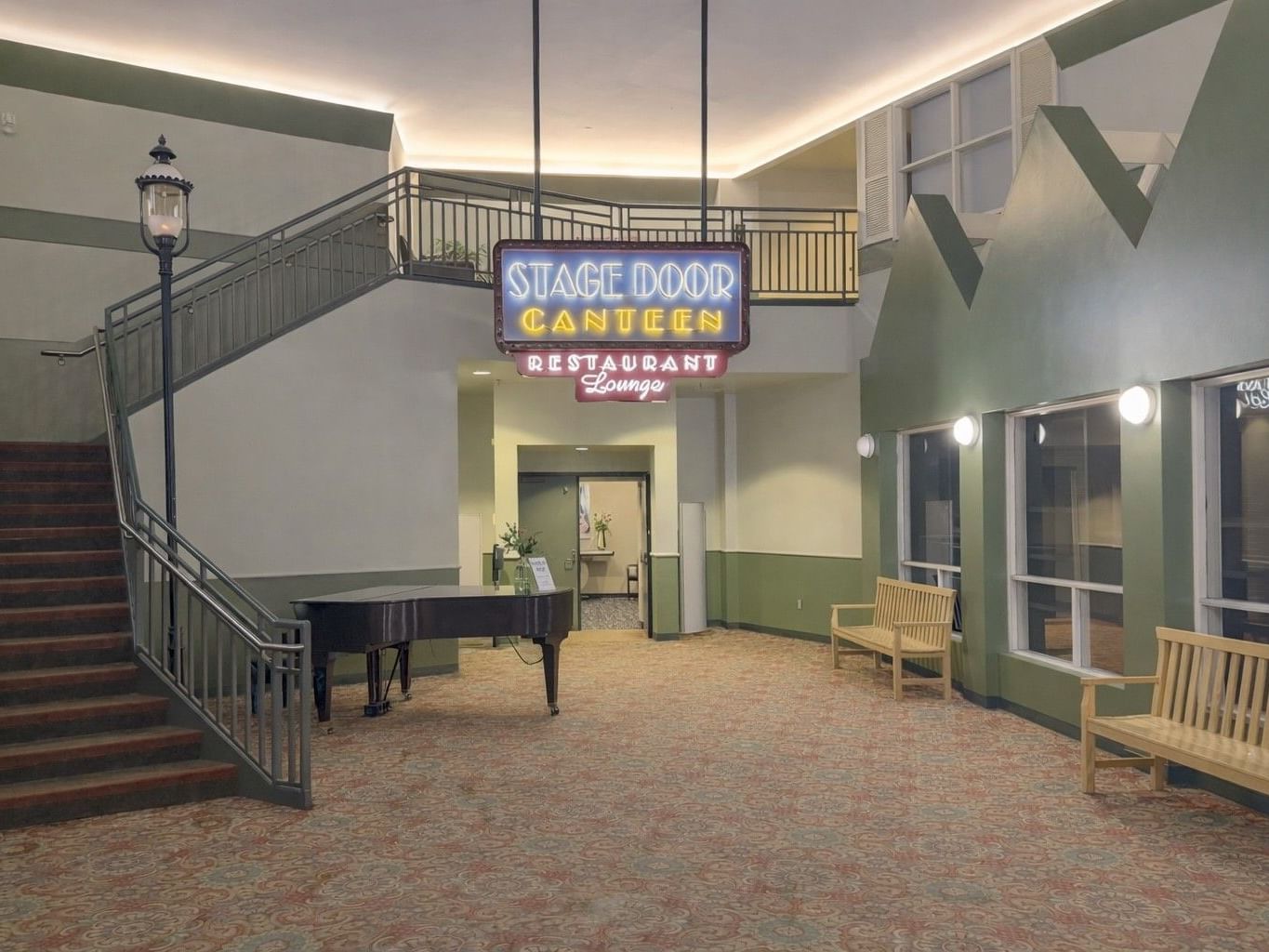 Indoor entrance to Stage Door Restaurant with a neon sign, grand piano, and staircase at Branson Hillside Hotel