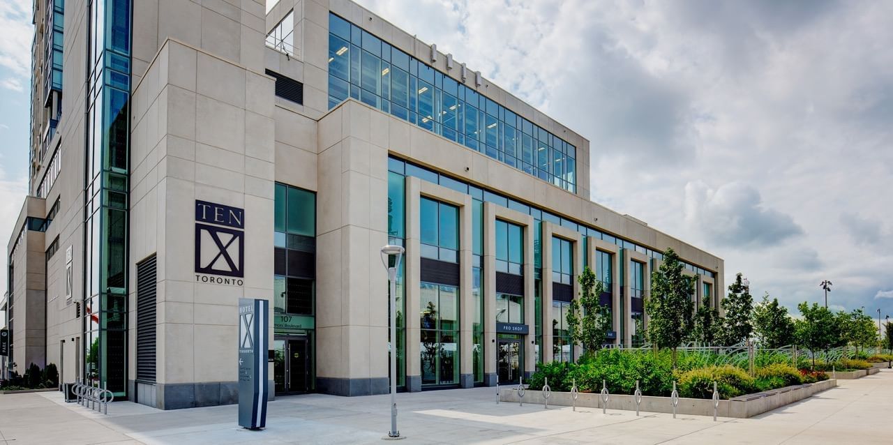 Vue extérieure de l'hôtel X Toronto avec sa façade en verre bleu et ses jardins paysagers