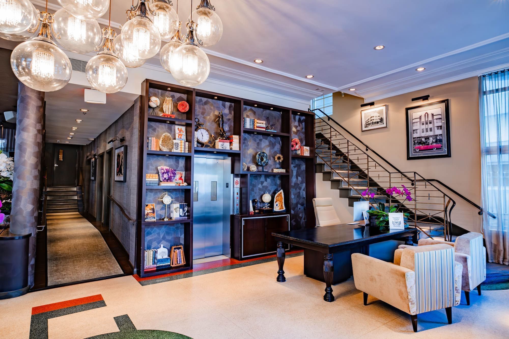 A hotel lobby with a staircase, bookshelf, and seating area.