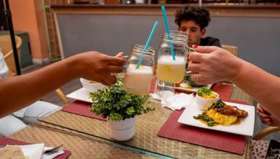 Two guests clinking mason jar cocktails over a restaurant table with food platters at Worthing Court Apartment