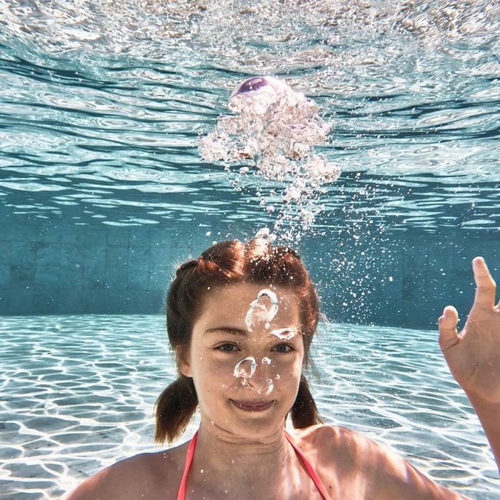 Unterwasseraufnahme einer Frau im Pool mit lachenden Gesichtsausdruck bei Falkensteiner Family Resort Sicily
