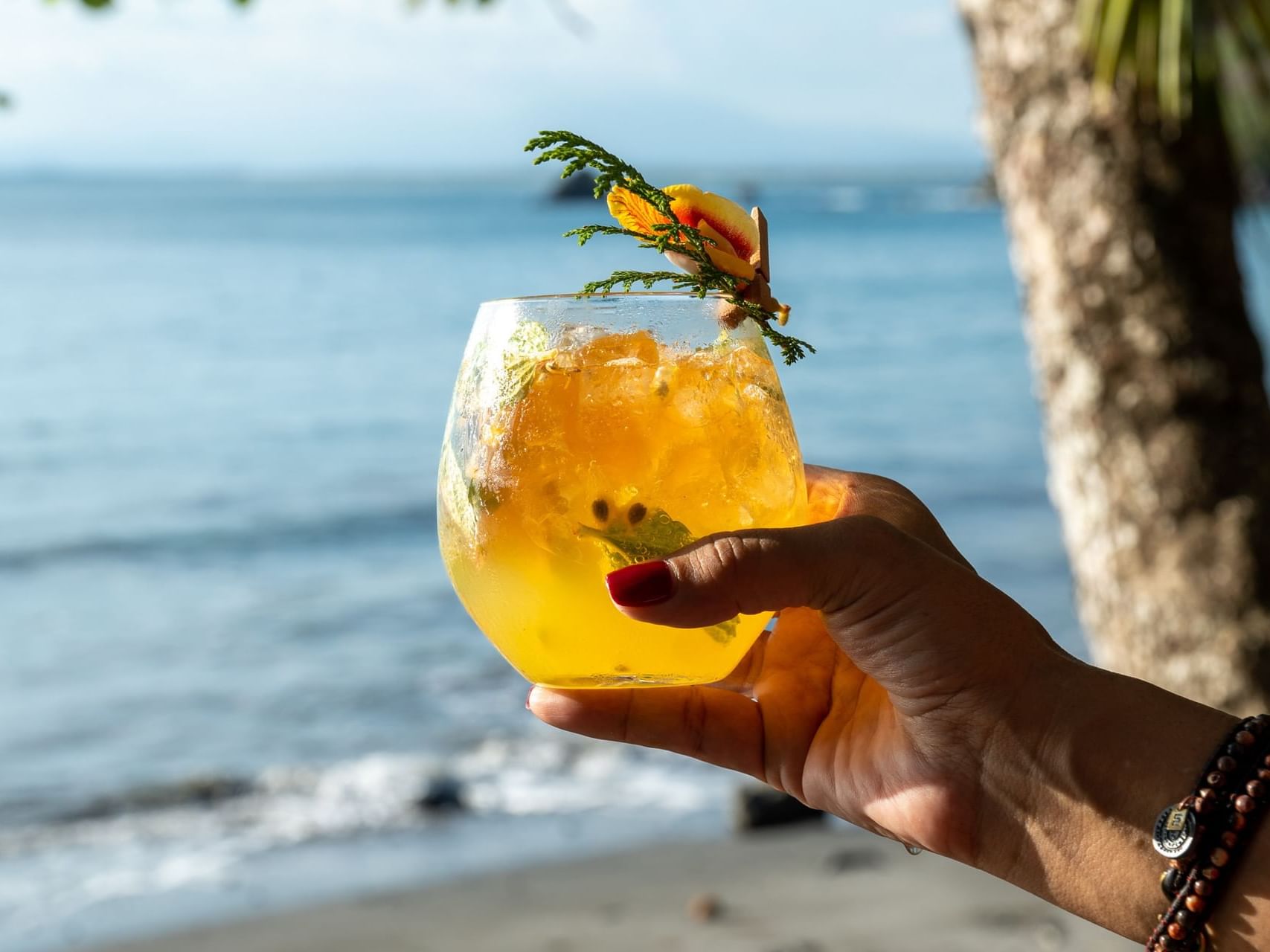 Persona levantando una copa de cóctel en la playa de Los Altos Resort