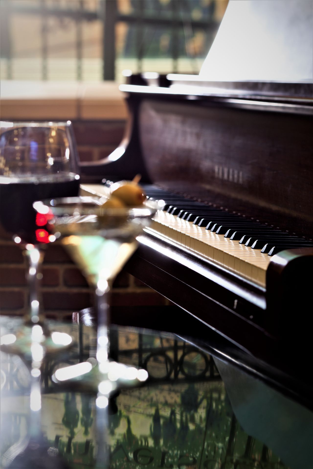 A close-up of a piano with two glasses of drinks on a glass table.