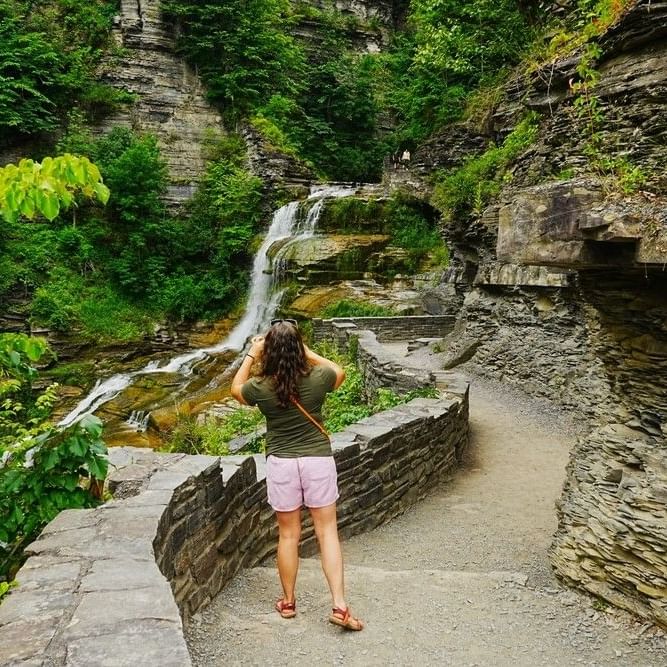 Tourist taking a photo of a waterfall cascading down a rocky gorge with green trees at La Tourelle Hotel and Spa