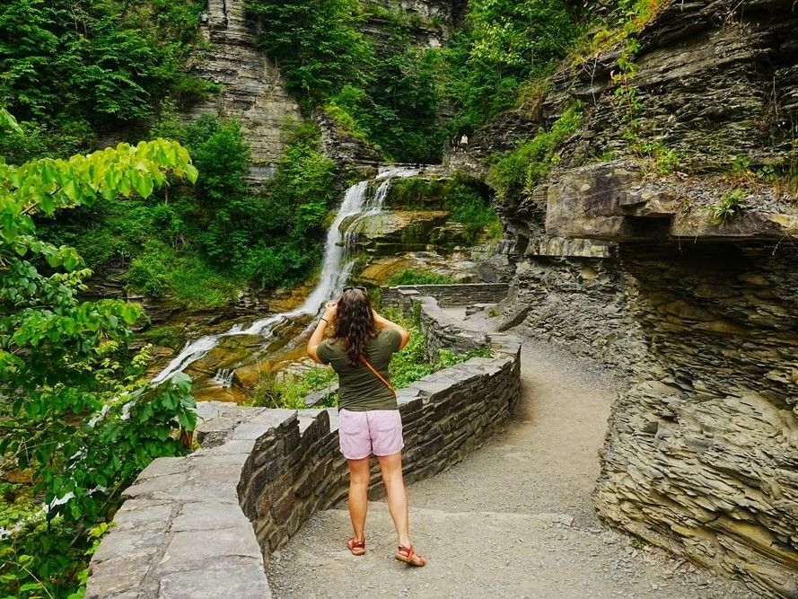 Tourist taking a photo of a waterfall cascading down a rocky gorge with green trees at La Tourelle Hotel and Spa