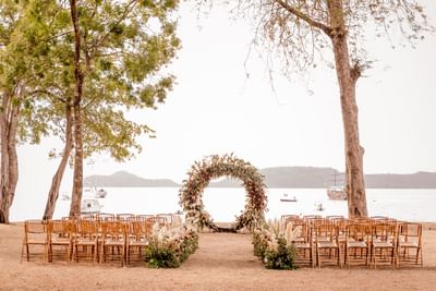 Outdoor wedding setup on a beach with chairs and a floral arch at El Mangroove Hotel