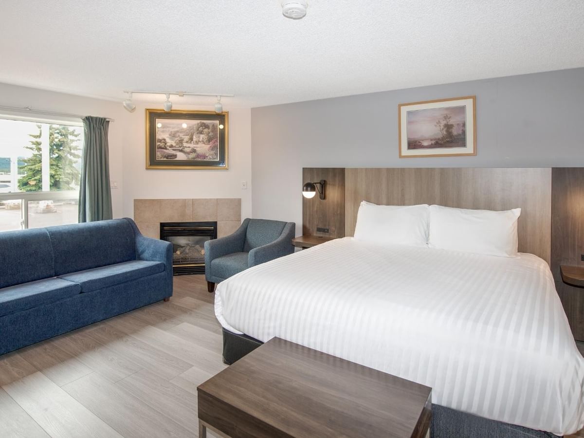 Hotel room with bed, couch, chair, fireplace, two framed pictures, and large window.