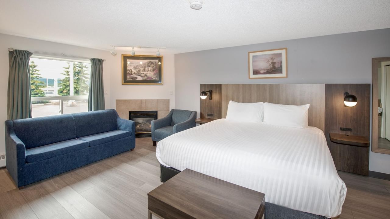 Hotel room with bed, couch, chair, fireplace, two framed pictures, and large window.