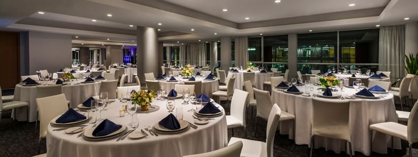 Round tables with white linens and blue napkins set by chairs in the Ballroom at Warwick Le Crystal Montreal