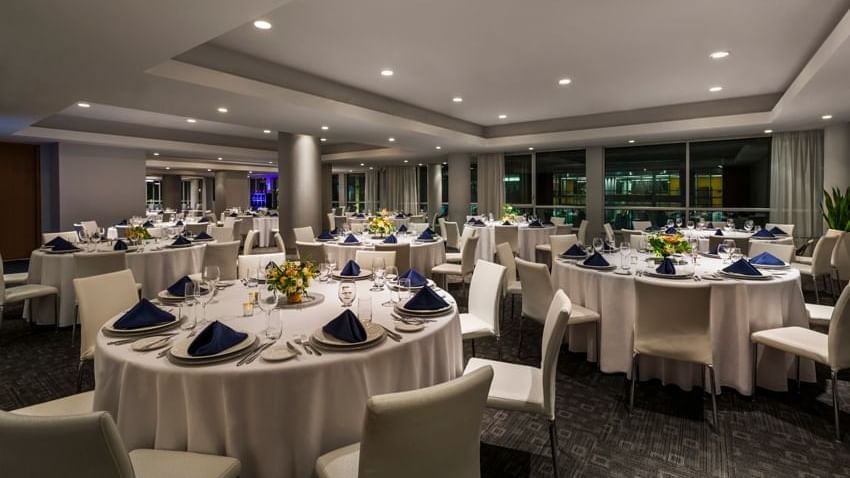 Round tables with white linens and blue napkins set by chairs in the Ballroom at Warwick Le Crystal Montreal