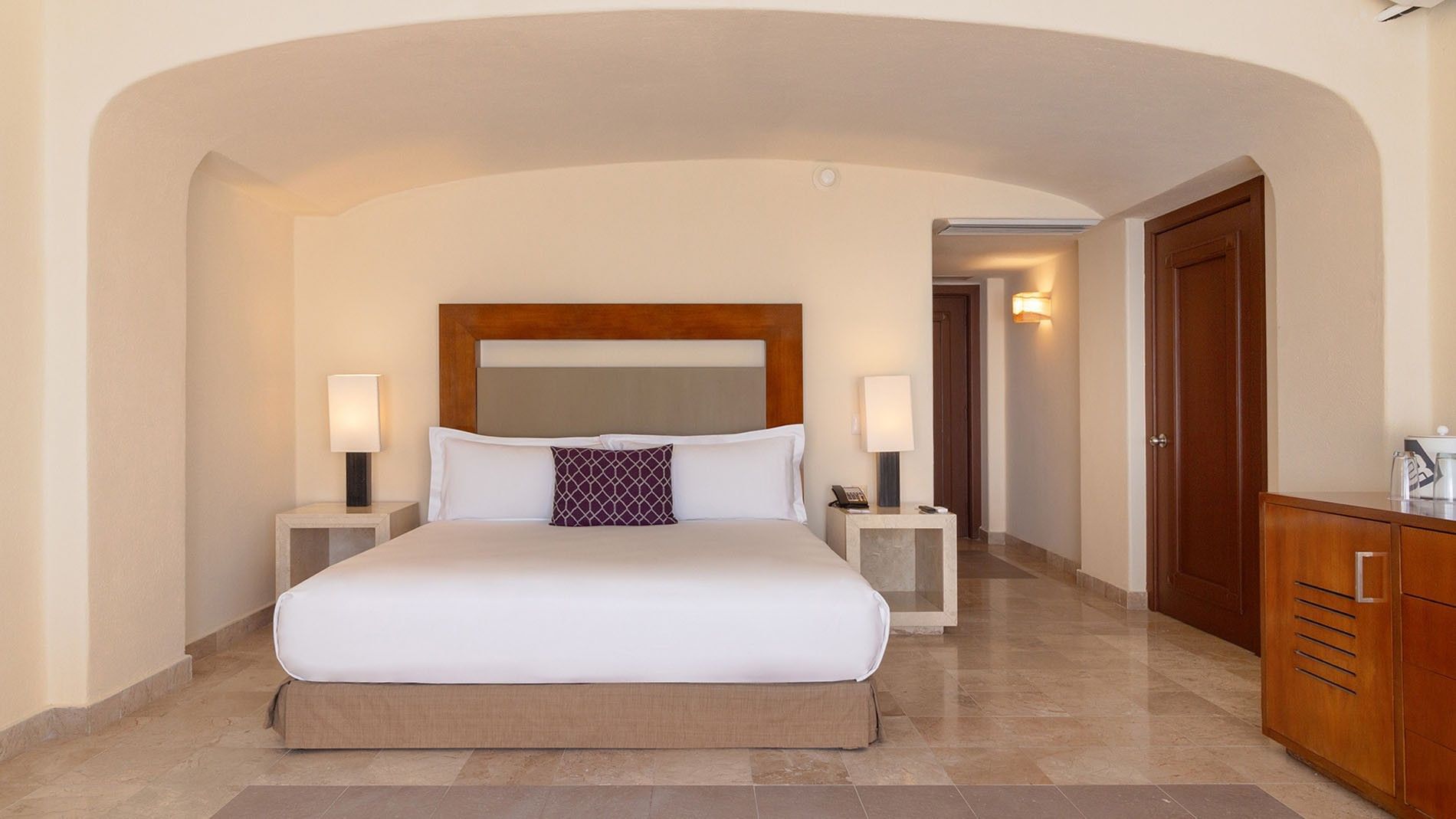 Nightstands by the bed with white linens in the Partial Ocean View Deluxe King Room at Camino Real Acapulco Diamante