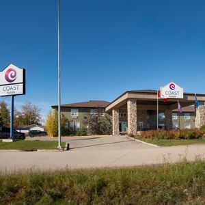 Modern two-story hotel building with stone pillars and Coast Hotels signage under a clear blue sky at Coast Edson Hotel.
