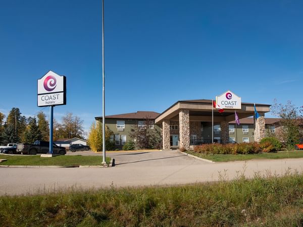 Modern two-story hotel building with stone pillars and Coast Hotels signage under a clear blue sky at Coast Edson Hotel.