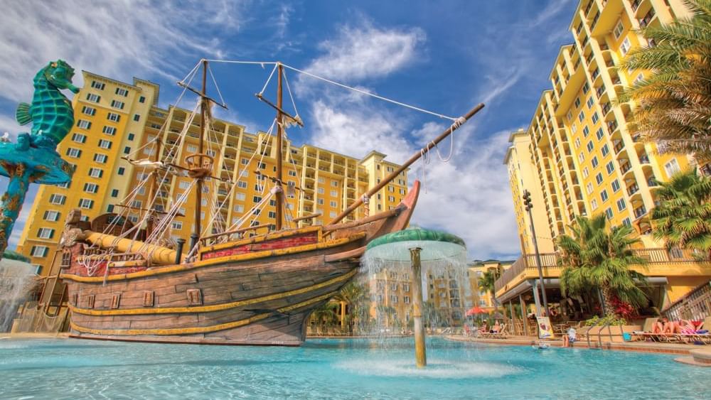 A large pool with a pirate ship fountain and buildings in the background.