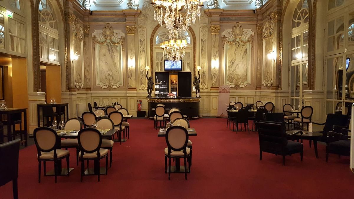 Intérieur élégant d'un restaurant avec tables, chaises, moquette rouge, lustres et bar.