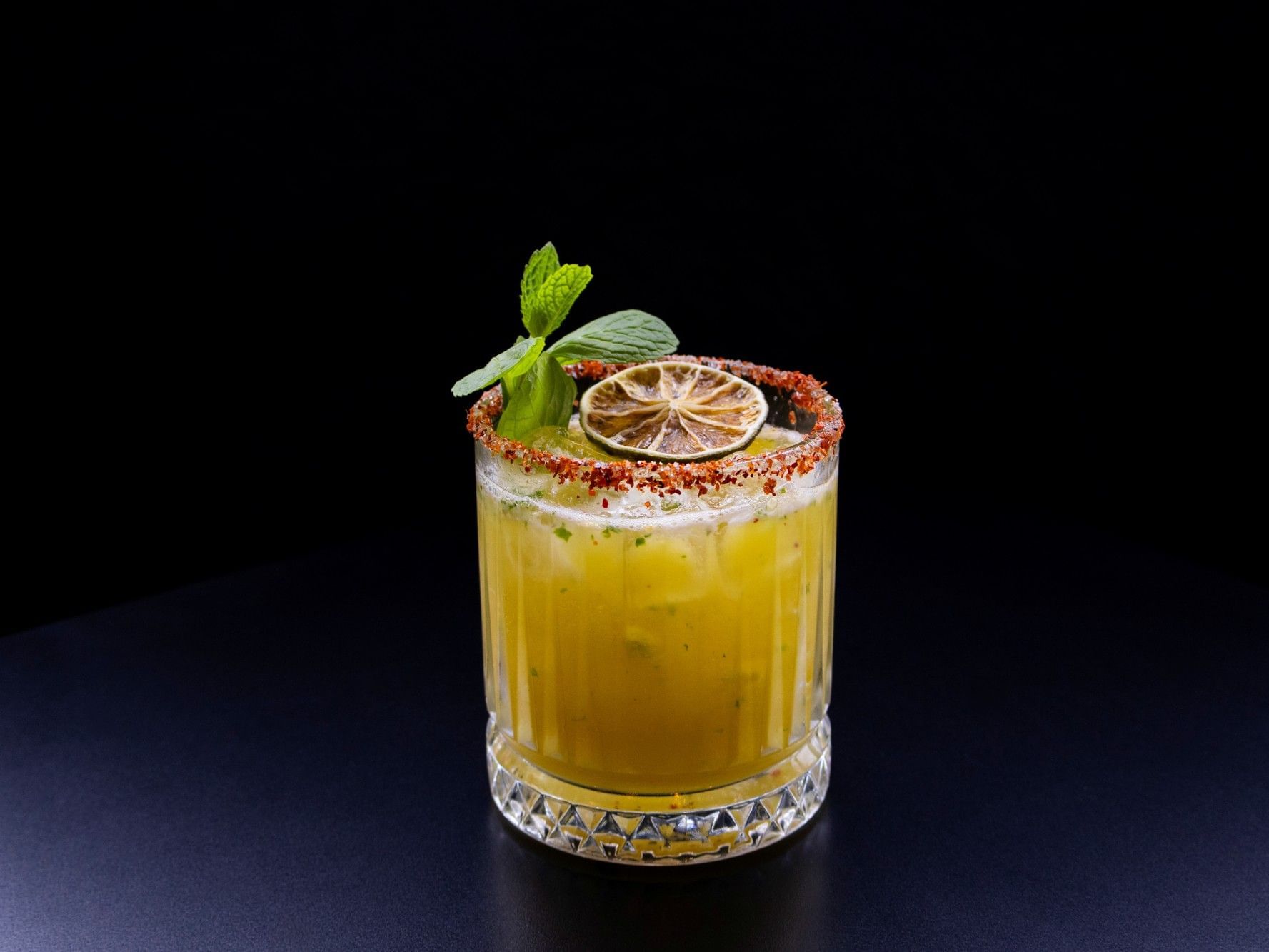 A vibrant yellow craft cocktail at Hotel Grand Chancellor Brisbane, featuring a spiced salt rim, fresh mint garnish, and a dehydrated lime slice in a crystal-cut glass.