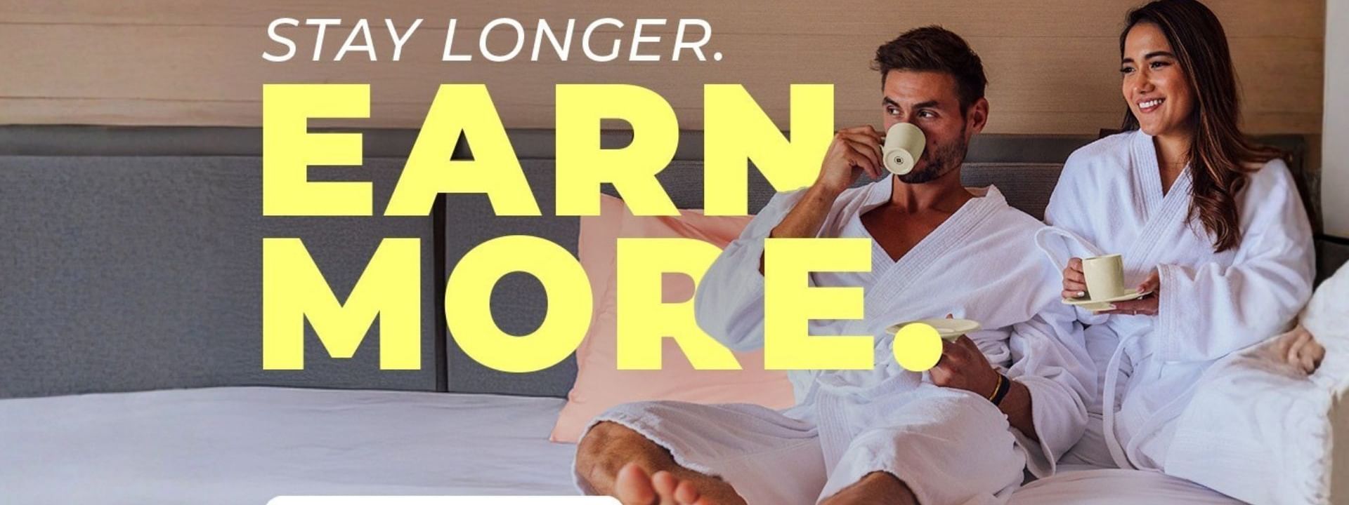 Couple in robes on a bed with the offer Stay longer. Earn more.