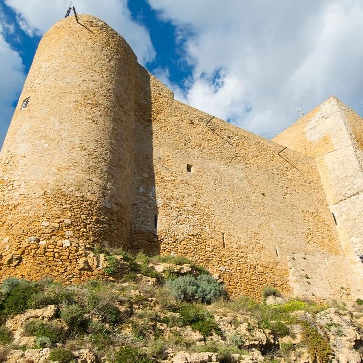 Antike Steinfestung auf einem Hügel mit zwei Laternen und blauem Himmel mit Wolken.