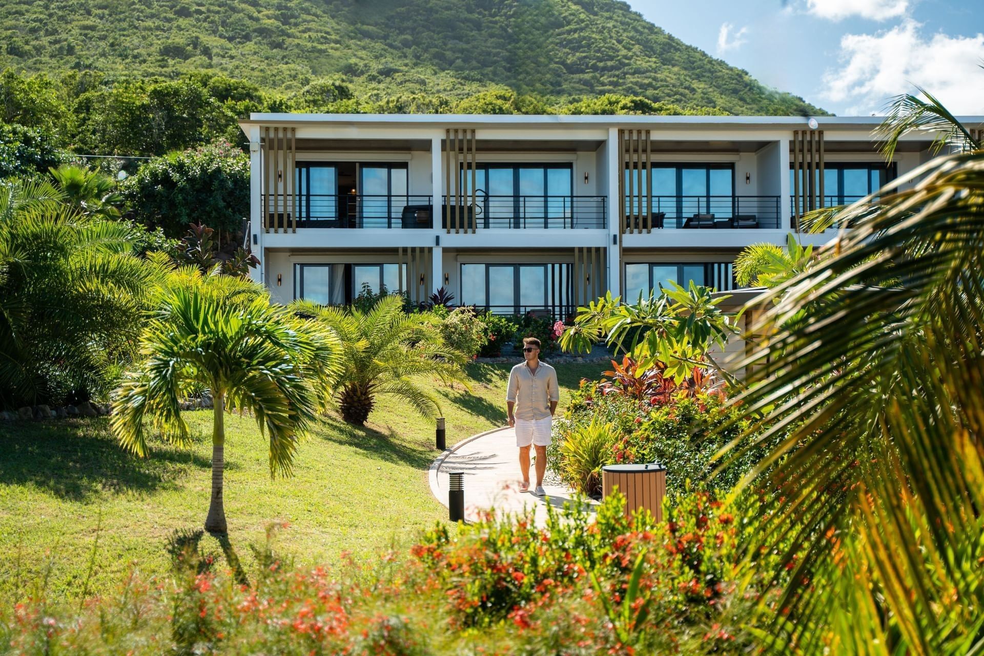 Modern suite buildings at Golden Rock Resort, surrounded by lush green tropical foliage, with a man walking along stone path
