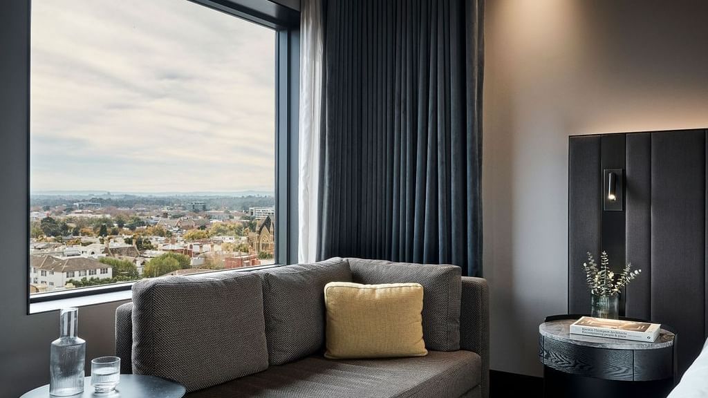 Superior room seating area with gray sofa, city views through windows at Pullman East Melbourne