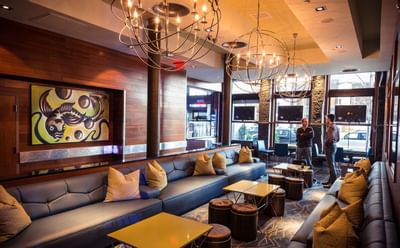 Lounge seating area with long couches and round tables beneath large spherical chandeliers at Harborside Inn Boston