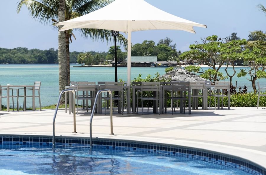 Outdoor pool with adjacent dining area under a large umbrella at Warwick Le Lagon - Vanuatu