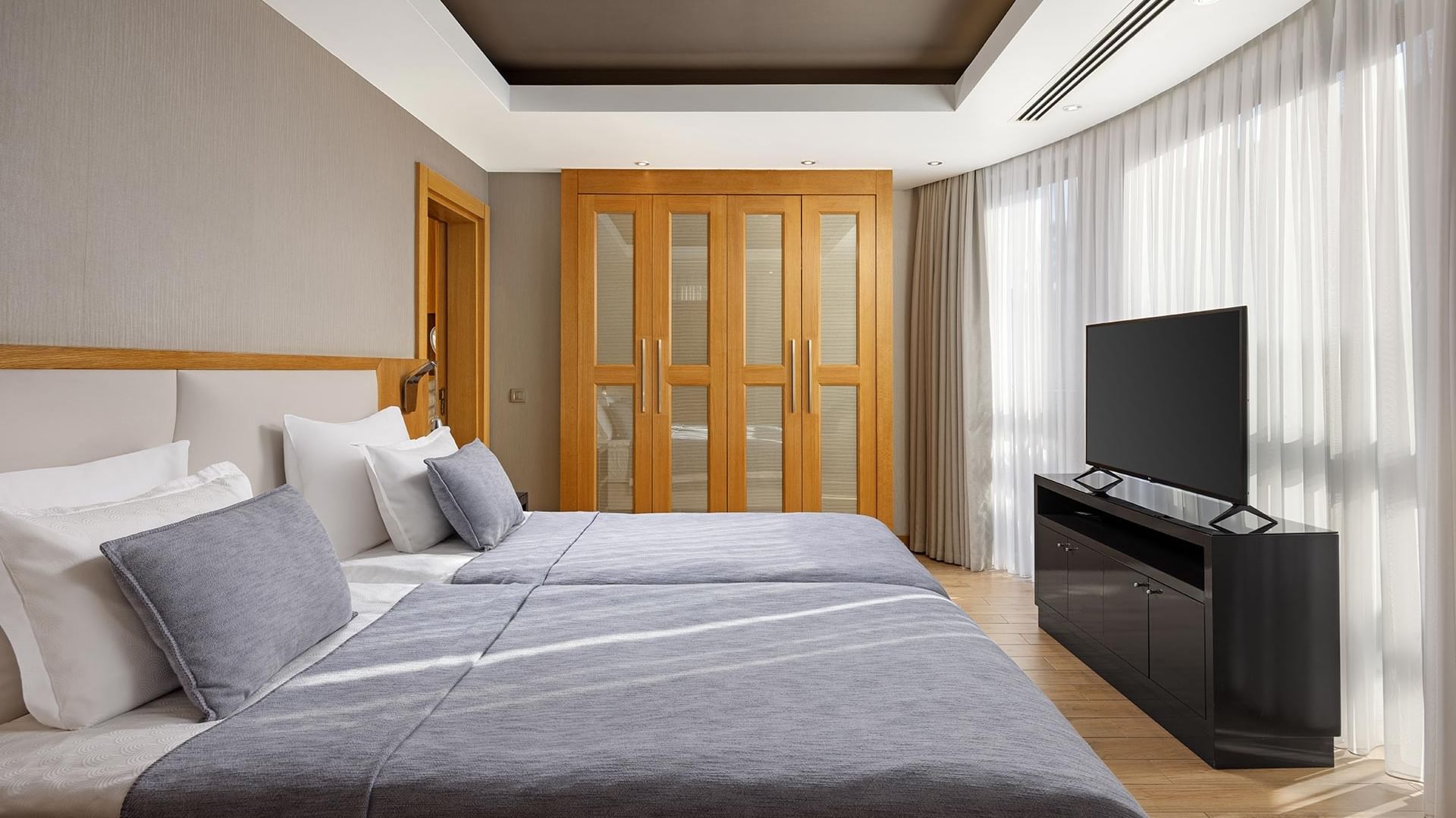 Спальня виллы Superior в Titanic Luxury Collection Bodrum с двумя кроватями, деревянным шкафом, телевизионной тумбой и большими окнами.