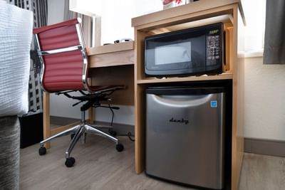 Microwave above a mini fridge beside a wooden work desk and red office chair in a bright guest room at Hotel Saint Clair