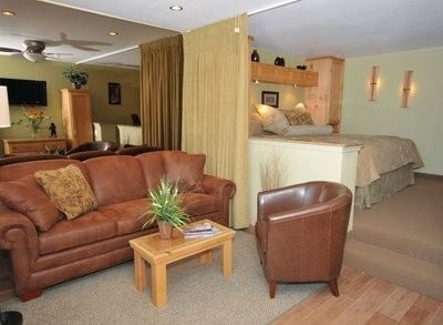 Deluxe Studio Suite with a leather couch and an elevated bedroom area separated by a partial wall at Americana Village Suites