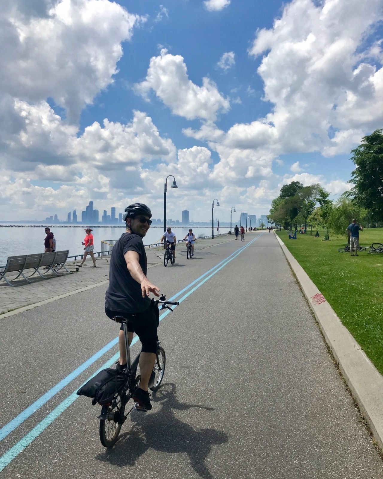 Cyclist riding by waterfront benches under cloudy skies with Toronto skyline views along a trail near Hotel X Toronto