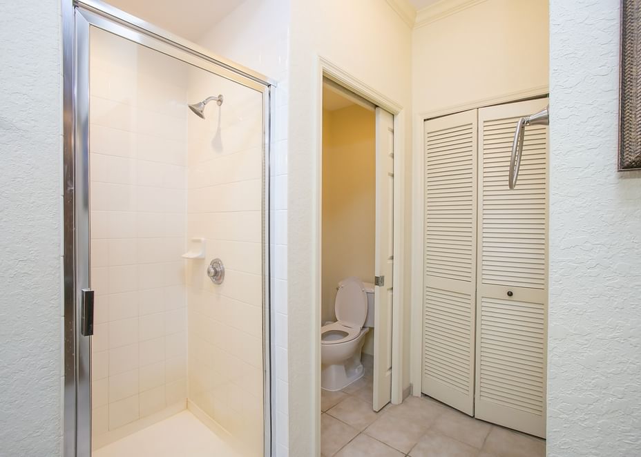 A bathroom with a tiled shower, toilet, and closet.