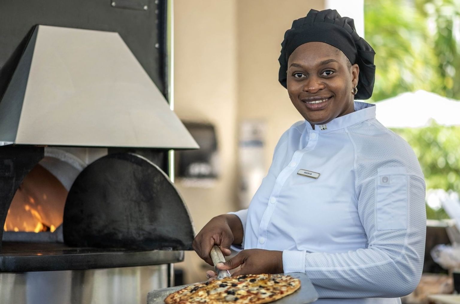 Smiling chef by a fired oven surrounding a pizza in Chickcharnie's Pizzeria & Grille at Warwick Paradise Island Bahamas