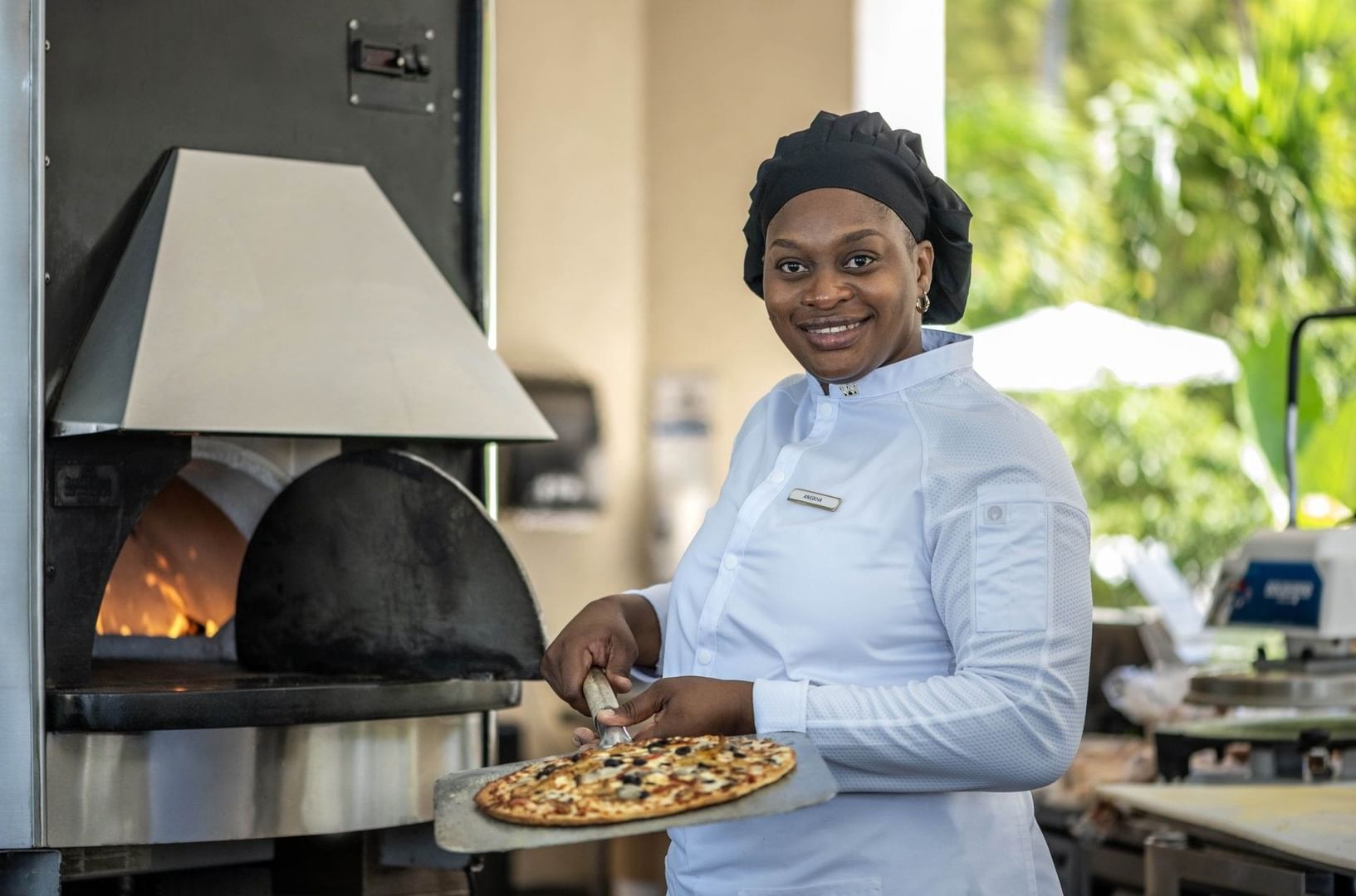 Smiling chef by a fired oven surrounding a pizza in Chickcharnie's Pizzeria & Grille at Warwick Paradise Island Bahamas