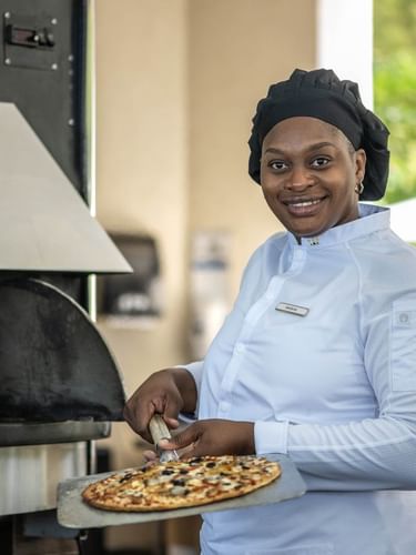 Smiling chef by a fired oven surrounding a pizza in Chickcharnie's Pizzeria & Grille at Warwick Paradise Island Bahamas