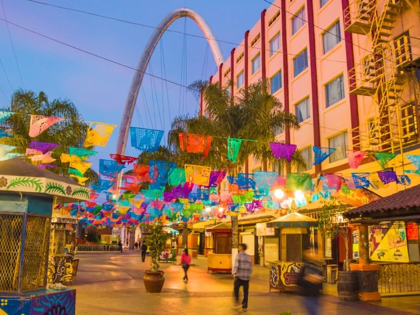 Calle de la ciudad con banderas coloridas y un gran arco metálico cerca de Camino Real Hotels