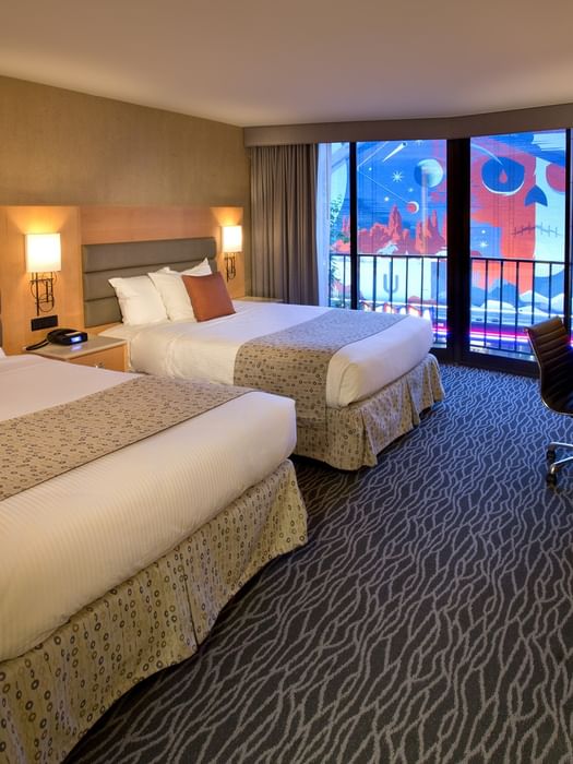 A hotel room with two beds, a nightstand, and a balcony with a city view.