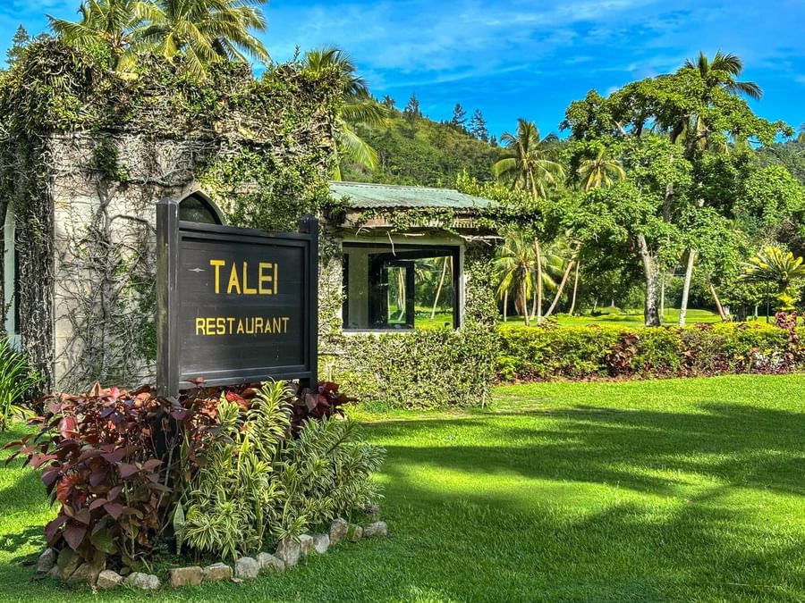 A sign for Talei Restaurant stands in lush greenery and tropical plants at The Naviti Resort.