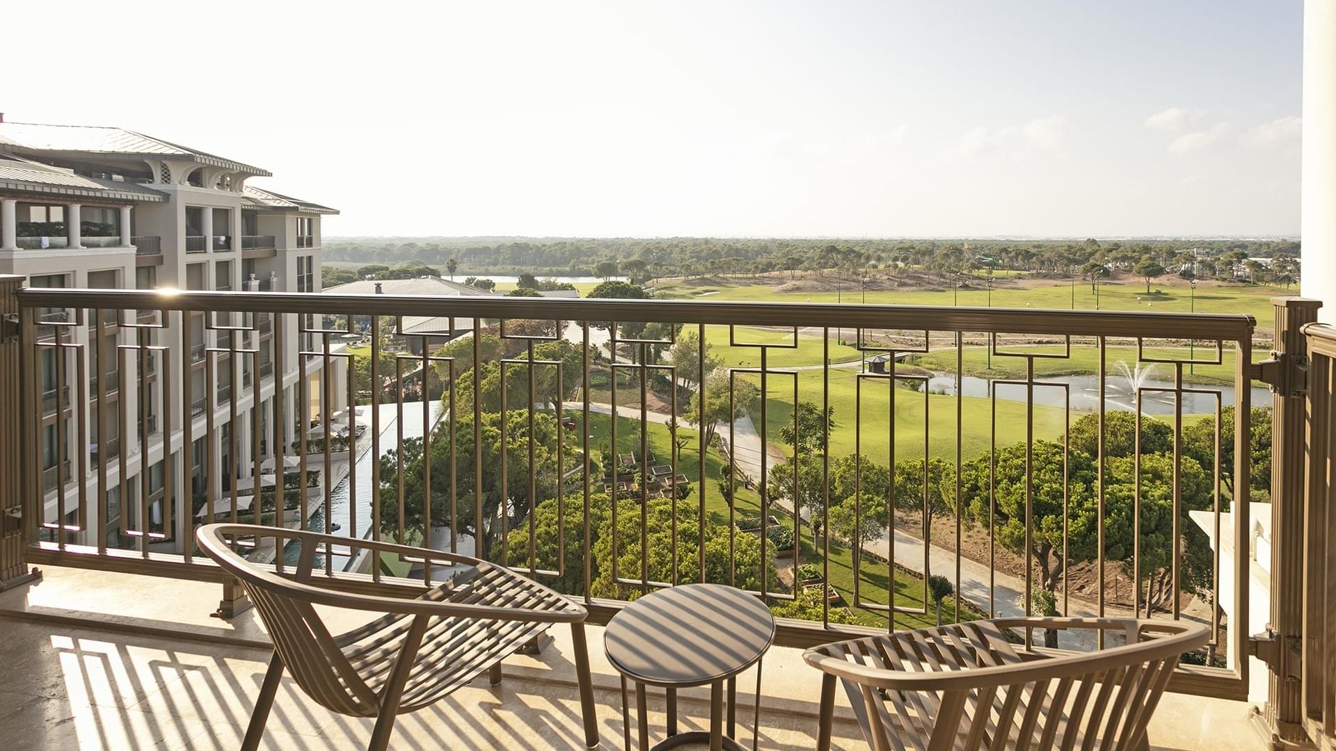 Balcony with chairs overlooking a golf course in Superior Room Golf View at Cullinan Belek