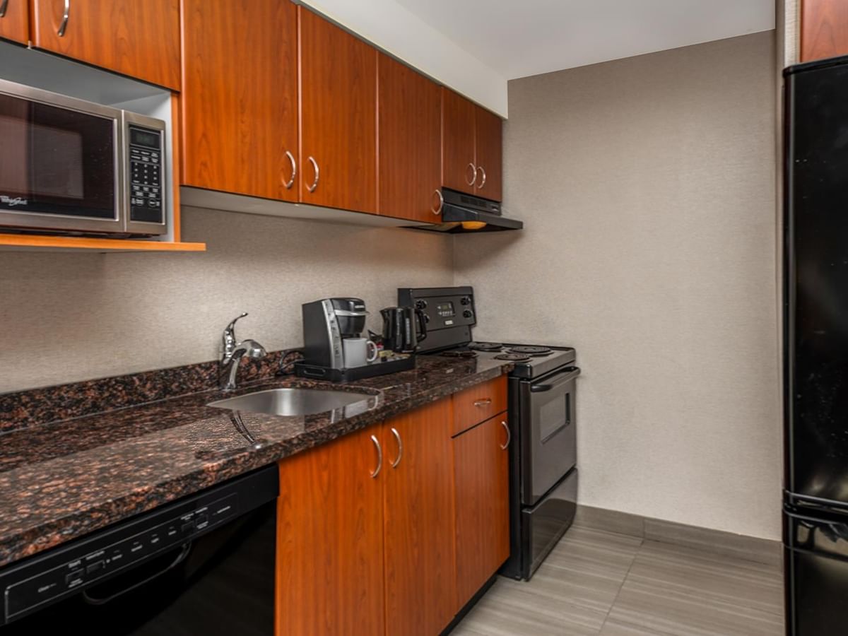 Hotel room kitchen with wooden cabinets, granite countertops, appliances, and coffee maker.