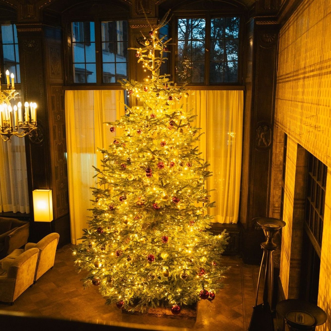 Festlich beleuchteter Weihnachtsbaum in einem eleganten Saal mit Kronleuchter und Kamin bei Christmas.